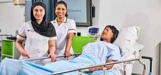 Two nursing students wearing scrubs, attending to a mock patient.