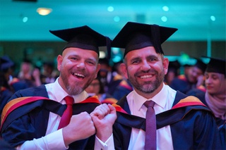 two smiling male graduates fist bump whilst looking at camera