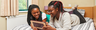Students in accommodation on a bed together looking at a tablet