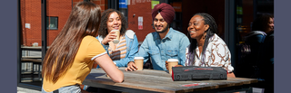 Four students with coffee sitting on a bench outside