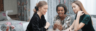 Three students sitting around a table and looking at a smartphone
