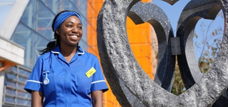 Photograph of Sabrina Ffrench in medical clothing standing in front of a sculpted heart