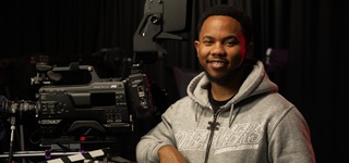 Photograph of Theo Johnson with a film camera on a darkened set
