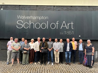 14 alumni line up underneath the 'School of Art' name outside the school