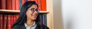 A student stood in front of a bookshelf smiling