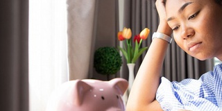 female student with head in hand looking worried, piggy bank on table
