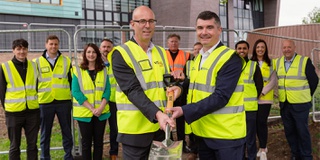 Phil Mottershead and Pete Cross hold up a spade with project team in background at decarbonisation ground breaking event at Walsall Campus