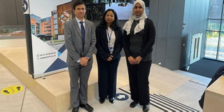 Three academic researchers stand in front of a promotional zap stand