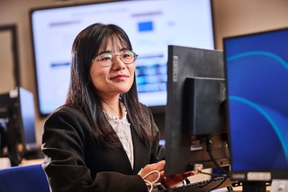 A smiling female student sits at a desktop computer in a computer lap