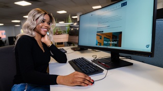 Smiling female student on a PC in the library visiting the University website