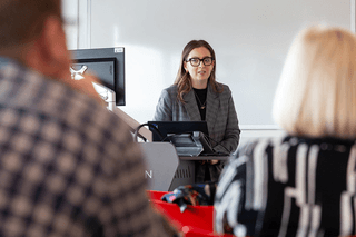 A presenter stands in front of audience in a class room