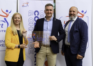Ross Cloak is flanked on the right by Prof Matt Wyon and on the left by Dr Kate Baker (Director of Performance and People at UK sport). They stand in front of a ETC backdrop. Ross is holding a glass award with the ETC logo in blue and red and the words Elite Training Centre in blue font.