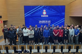 29 students and lecturers stand in line in a lecture theatre in front of a projector screen with a blue back ground and the words 'Valores De La21 RCD Espanyol 25-26' in white lettering.