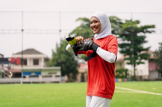 Young Muslim woman wearing a hijab and sportswear, removing goalkeeper gloves