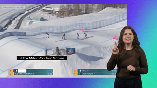 Olivia stands on the right of a large screen showing skiing at the Milan Cortina Games. She is using British Sign Language to interpret the commentary.