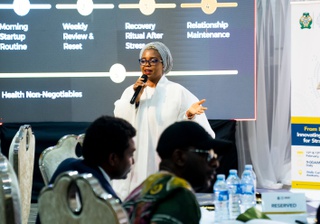 Sesi Oluwatoyin Orere speaks at an event. She has a white dress and headdress and addresses an audience