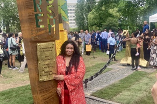 Victoria Murrain stands next to the monument she helped to create. She wears an orange suit and is surrounded by members of the community.
