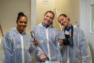 Anna Grey, Lily Simkin and Louanne Worsey dressed in overalls, ready for their investigation at Locard House. They hold a magnifying glass and a camera.