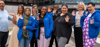A photograph of all our university Wellbeing Champions. Image is taken outside of the Alan Turing Building. Everyone is happy and smiling