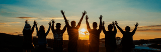 Students silhouetted against a setting sun, raising their arms together