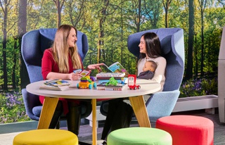 Staff and student sitting and talking, student holding baby doll with books on table in front