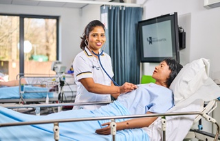 Female student standing over dummy checking chest with stethoscope