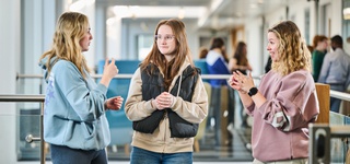 Photograph of three students in the Business School conversing through sign language.