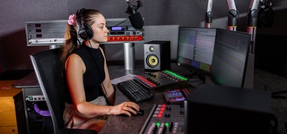 Female student sat operating the control desk in the radio studio. She is wearing headphones focussing on the audio levels