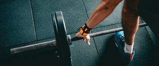A person at the gym preparing to lift a barbell weight: they are wearing an armband and blue shoes