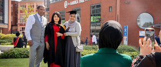 A graduate in robes and their parents posing for an iPhone photograph