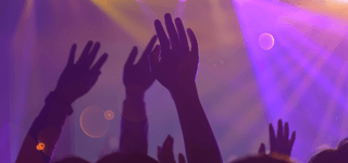 Silhouettes of raised hands at a nightclub, illuminated by purple lights