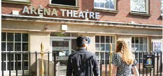 Two students outside the Arena Theatre, facing the entrance with Arena Theatre displayed in its signage above the door