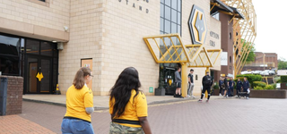 Two students walking outside the Molineux Stadium, the logo for Wolverhampton Wanderers displayed on the side of the building
