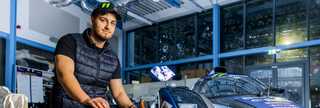 UWR student sitting in front of a race car