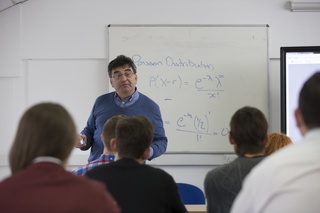 Equations wrote on white board with lecture standing in front teaching to the class