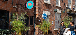 Two students walking through shops in Wolverhampton, passing a sign reading GRAIN STORE