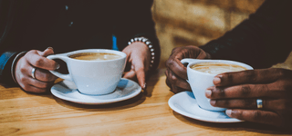 Two coffee cups on saucers placed on a table and held by two students