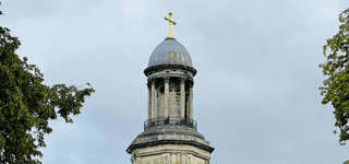 The top of a tower, small pillars leading to a round, sloped roof with a golden cross at its peak