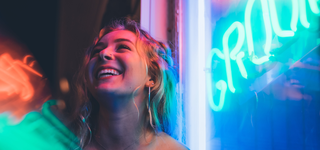A woman standing by a large window in the light of a neon sign at night