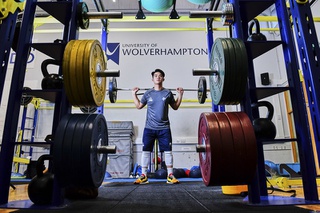 A student in the gym at City Campus, in uniform and lifting weights in the free weights suite