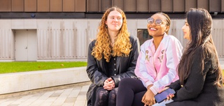 Three students sitting in the courtyard in front of the Alan Turing building.