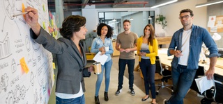 A person drawing on a whiteboard for a group of onlookers.