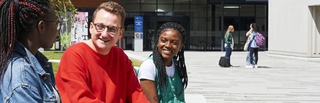 Three students sitting and conversing in the City Campus courtyard, with two more students in the background near the Millennium City Building entrance