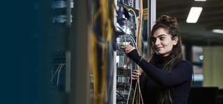 A female student with brown hair and wearing a blue jumper working on a network switch.