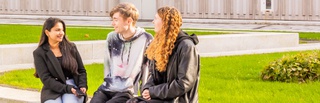 Three students, one male and two female sitting chatting in the courtyard at the University of Wolverhampton's City Campus in the sunshine.
